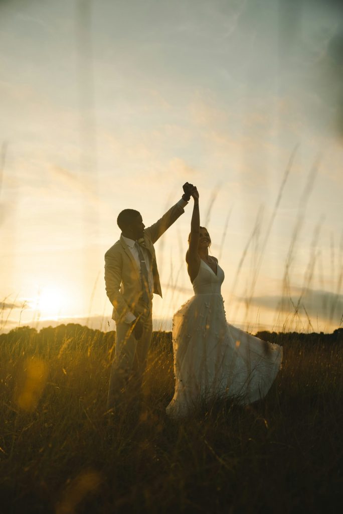 un couple de mariés dansant dans un champ au coucher du soleil
