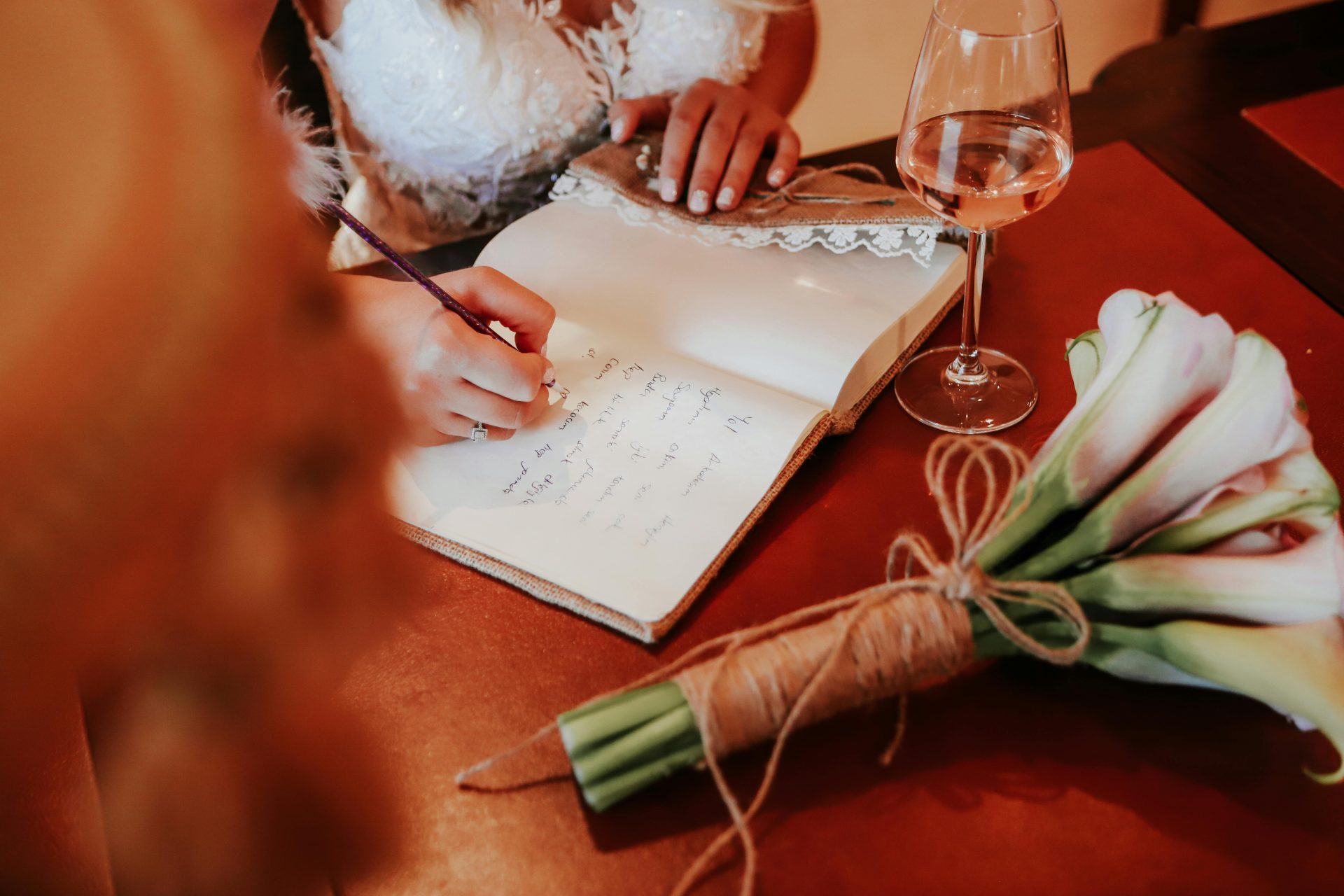La mariée écrit dans un journal, un bouquet de fleurs et un verre de vin à la main, immortalisant un moment de mariage serein.